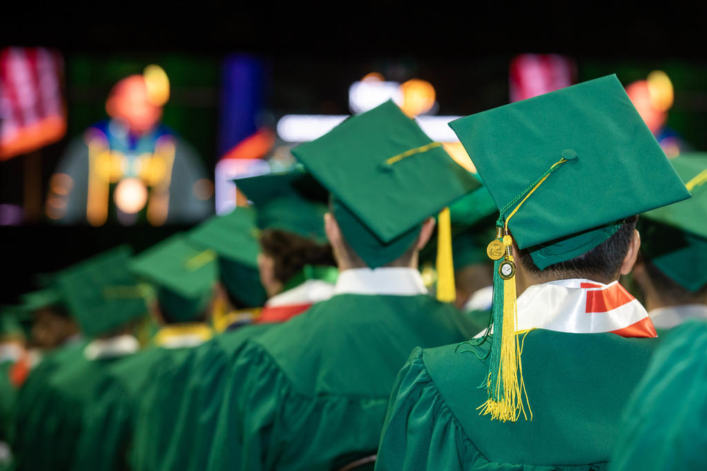Rear view of group of people wearing green graduation caps and gowns.