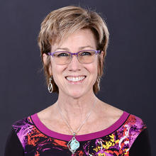 Smiling woman with short brown hair wearing glasses.